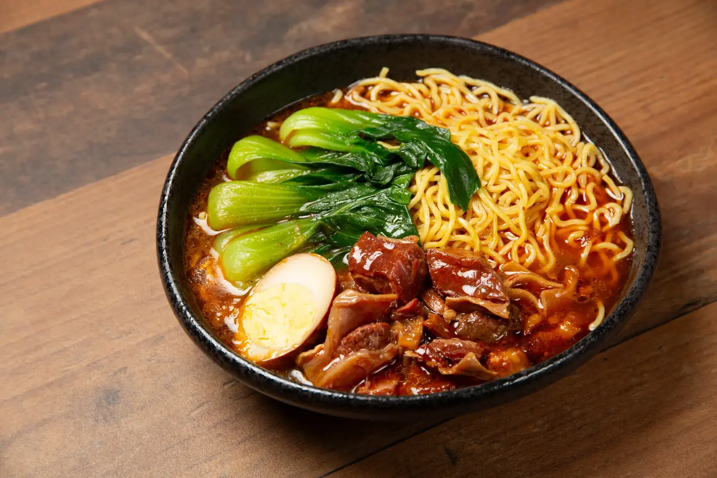 Braised beef noodle bowl topped with greens and pickled vegetables